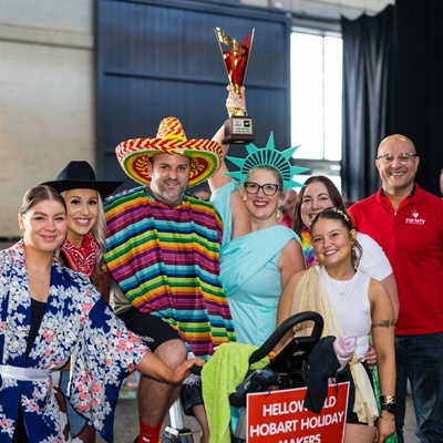 people dressed in outfits from all around the world including Mexico, greece, japan and New York holding a trophy on their spin bike