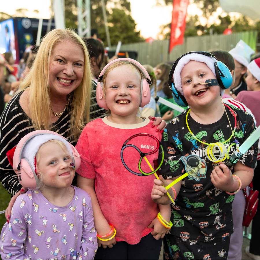 blond woman and three kids smiling and enjoying the carols. The two girls have noise-cancelling headphones and the boy has a feeding tube.